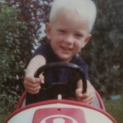 John as a child riding in a toy car